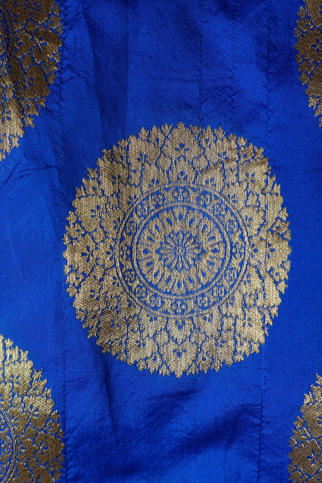 A close-up of a royal blue fabric with a large circular gold brocade motif and partial matching motifs at the edges.