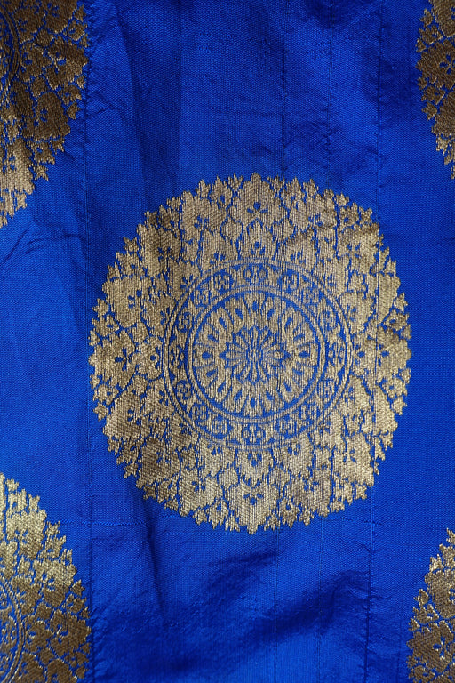 A close-up of a royal blue fabric with a large circular gold brocade motif and partial matching motifs at the edges.